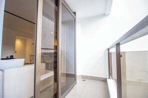 A modern interior with a glass door leading to a bathroom, a white sofa, and a small seating area with chairs. - Classic by Bhomy (São Paulo)