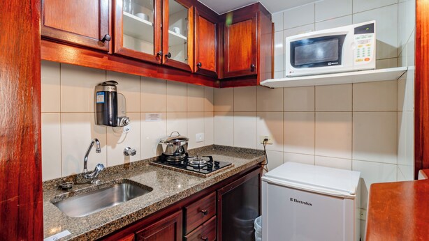 A kitchen with wooden cabinets, a stainless steel sink, a built-in microwave, and a white dishwasher. - Classic by Bhomy (São Paulo)