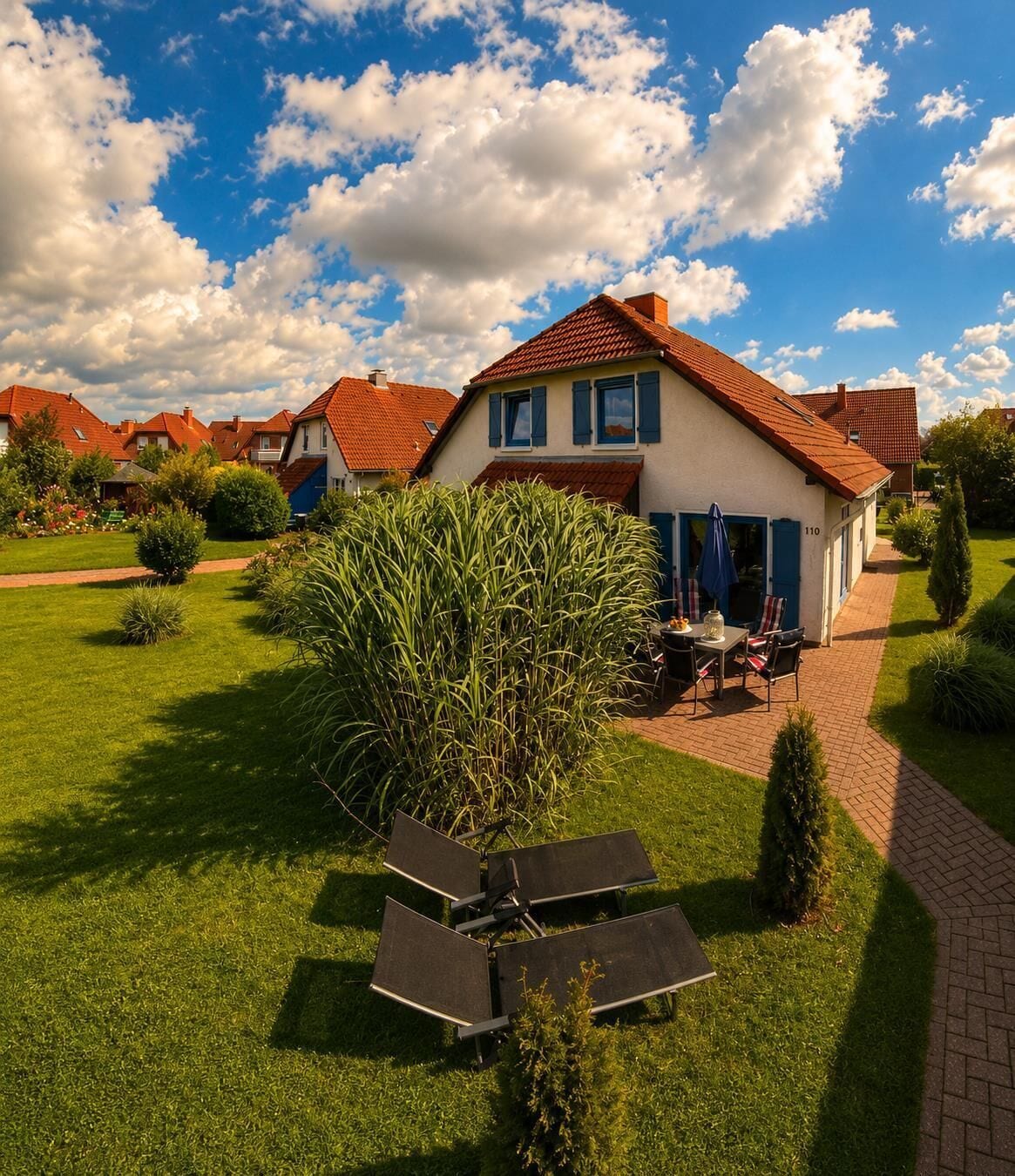 A residential property with a well-maintained lawn, a patio with outdoor furniture, and a house with a red-tiled roof.