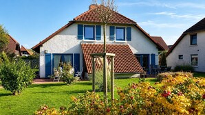Ein zweistöckiges Haus mit rotem Ziegeldach, einem kleinen Garten mit Blumen und einer Holz-Pergola.