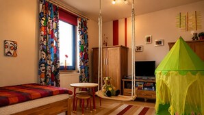 Ein Schlafzimmer mit einem Bett, einem Schaukelstuhl, einem grünen Zelt, einem Fernseher und einem Fenster mit Vorhängen.