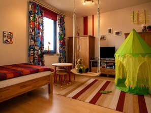 Ett sovrum med en säng, en gungstol, ett grönt tält, en tv och ett fönster med gardiner.
