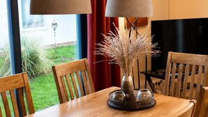 Ein Essbereich mit Holztisch, Stühlen, einer Vase mit Trockenpflanzen und zwei Pendelleuchten.
