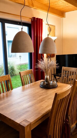 En matplats med ett träbord, stolar, en vas med torkade växter och två hänglampor.
