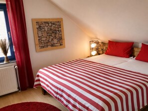 Ein Schlafzimmer mit einem Bett, roten Vorhängen, einer Wanddekoration aus Stein und einem Nachttisch mit Lampen.