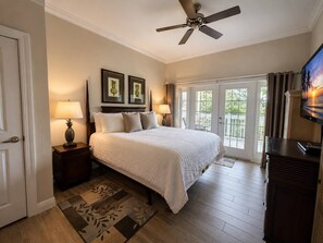 A bedroom with a bed, two bedside lamps, a ceiling fan, a television, and a view through a glass door. - Luxury 3BR Reunion Condo Golf Views Near Disney (Kissimmee)