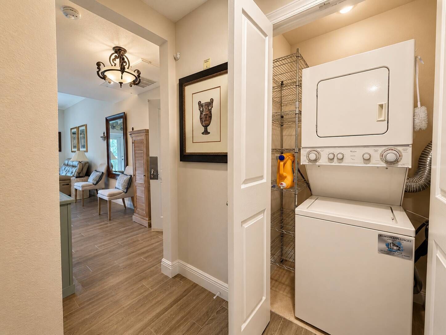 A laundry room with a front-loading washer and dryer, a metal drying rack, and a framed picture on the wall.