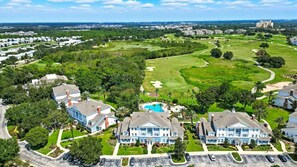 A residential area with multiple two-story houses, a golf course, and a large building in the background. - Luxury 3BR Reunion Condo Golf Views Near Disney (Kissimmee)