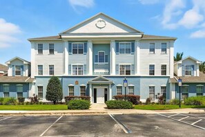 A multi-story building with a central entrance, a wheelchair accessibility sign, and a parking lot in front. - Reunion Resort 3BR | Beautiful Views + Pool Access (Kissimmee)