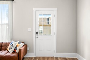 A white door with a window, a brown leather sofa with patterned cushions, and a wooden floor. - Roadmap Lodging: Solo Traveler 1BR, Own Entrance (Columbus)