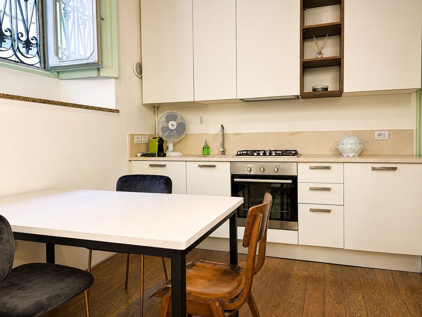 Een kleine keuken met een eettafel, stoelen, een fornuis en een ventilator.