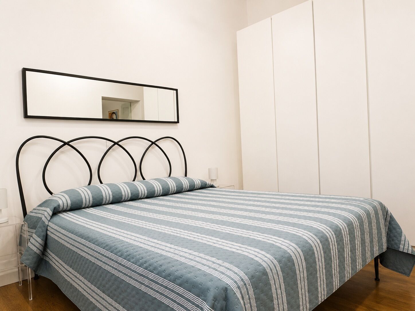 Une chambre à coucher avec un lit, une table de chevet, une lampe, une armoire et un miroir au mur.