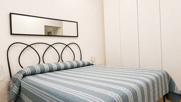 Une chambre à coucher avec un lit, une table de chevet, une lampe, une armoire et un miroir au mur.