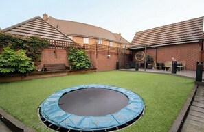 Ein Garten mit Trampolin, einem Ziegelhaus und einer Terrasse mit Gartenmöbeln.