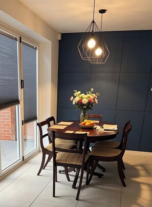 Een eetgedeelte met een donkerblauwe wand, een ronde houten tafel en stoelen met beklede zitplaatsen.