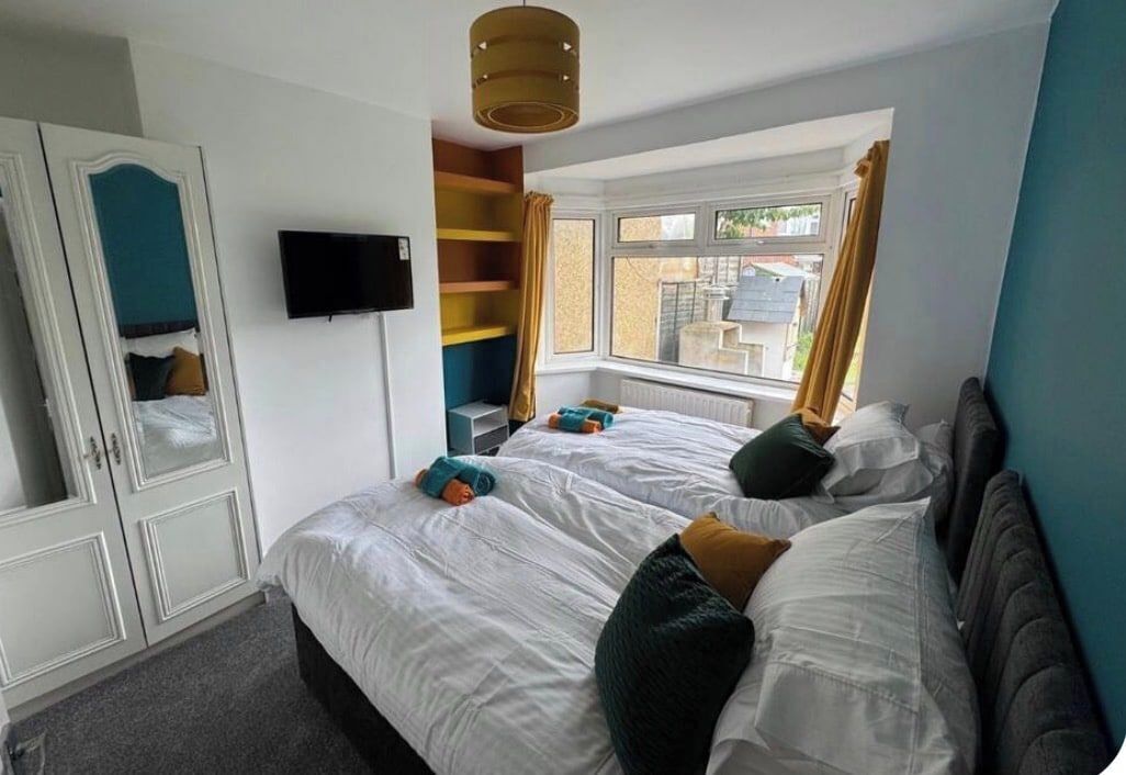 A bedroom with two beds, a wardrobe, a television, and a window with curtains.