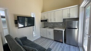 Cocina compacta con armarios blancos, horno empotrado y refrigerador de acero inoxidable.