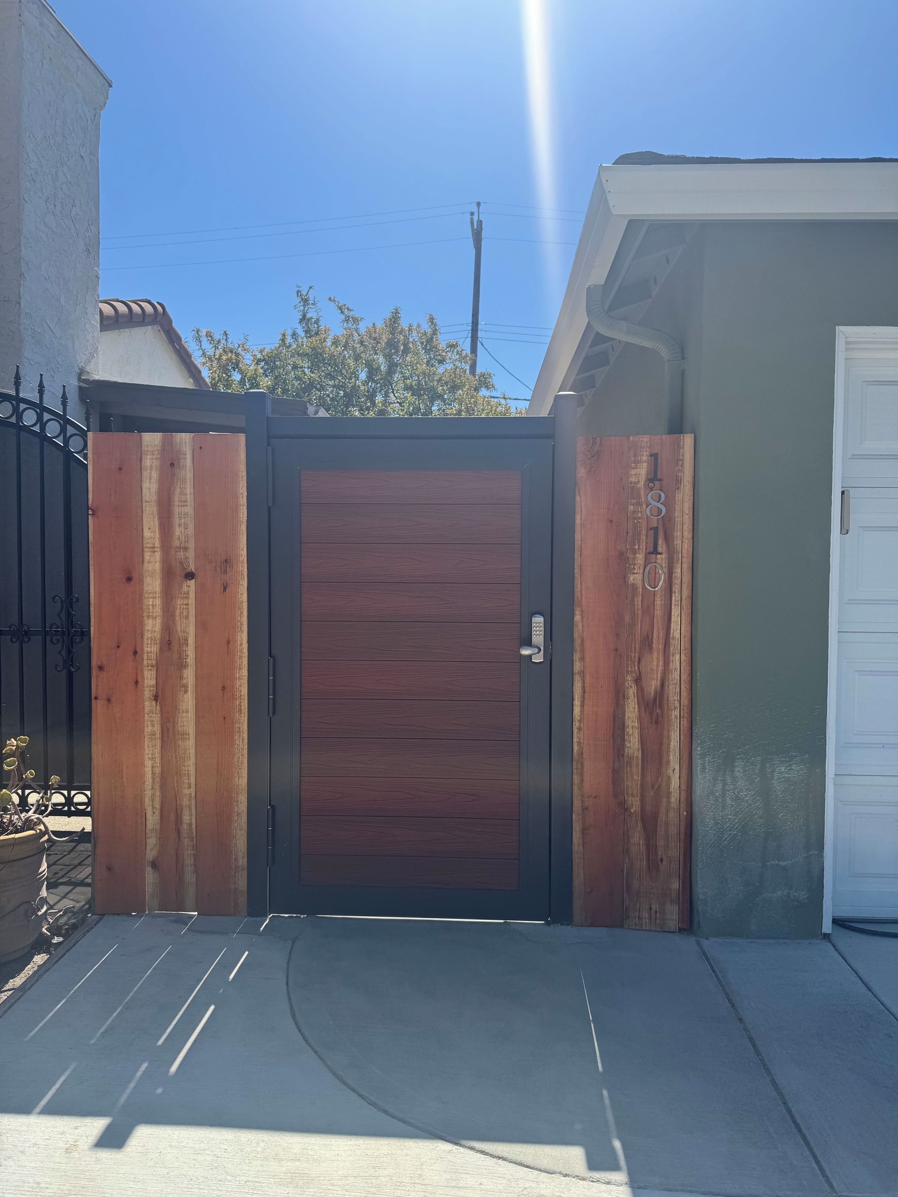 A gated entrance with a wooden door, a concrete driveway, and a white garage door.