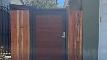 A gated entrance with a wooden door, a concrete driveway, and a white garage door.
