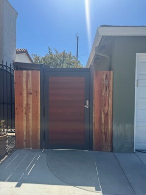 Une entrée fermée par un portail et une porte en bois, une allée en béton et une porte de garage blanche.