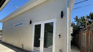 Un edificio con puerta corredera de vidrio, una ventana pequeña y un escalón de hormigón que conduce a la entrada.