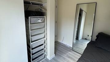 Makuuhuone, jossa on sänky, vaatekaappi, jossa on tilaa vaatteiden ripustamiseen, peili ja ovi, joka johtaa toiseen huoneeseen.