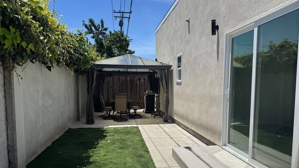 Un jardín trasero con un patio, una zona de estar cubierta y un césped.
