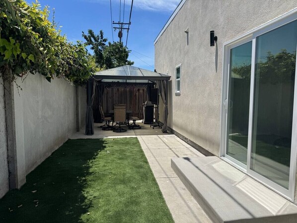 Un jardín trasero con un patio, una zona de estar cubierta y un césped.