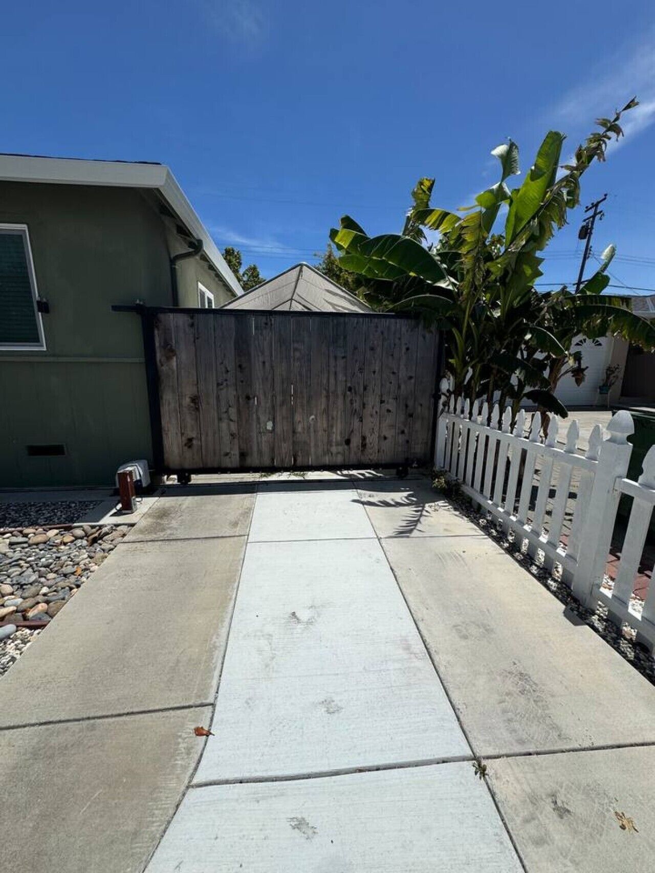 Um imóvel residencial com entrada por calçada de concreto, cerca de madeira e cerca branca de piquete.