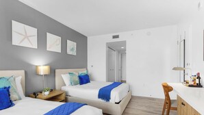 A hotel room with two beds, a desk, a chair, and artwork on the walls. - 2BR Intracoastal Retreat - Private Balcony (Hallandale Beach)