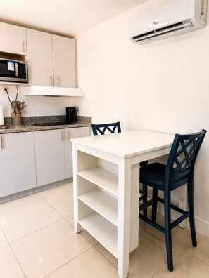 A kitchen with white cabinets, a microwave, a coffee maker, and a white dining table with a chair. - Cozy Poolside Guest House-Gazebo + Free Parking (West Park)