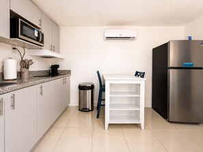 Une cuisine moderne équipée d’un four à micro-ondes, d’un climatiseur, d’un réfrigérateur en acier inoxydable et d’une table blanche avec des chaises bleues.
