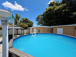 A swimming pool with a ladder, surrounded by a wooden deck and a covered area. - Cozy Poolside Guest House-Gazebo + Free Parking (West Park)