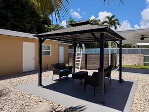 A covered outdoor seating area with chairs and a table, a ladder, and a door. - Cozy Poolside Guest House-Gazebo + Free Parking (West Park)