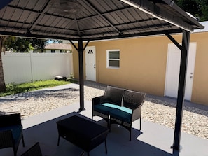 An outdoor patio with a covered seating area, a white door, and a white fence in the background. - Cozy Poolside Guest House-Gazebo + Free Parking (West Park)