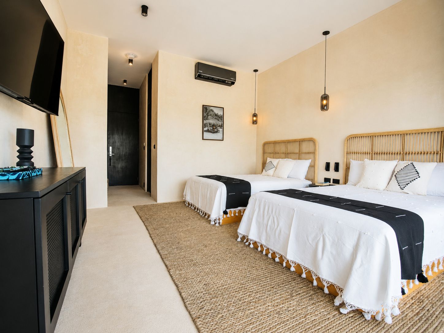 A hotel room with two beds, a television, a desk, and a door leading to another room.