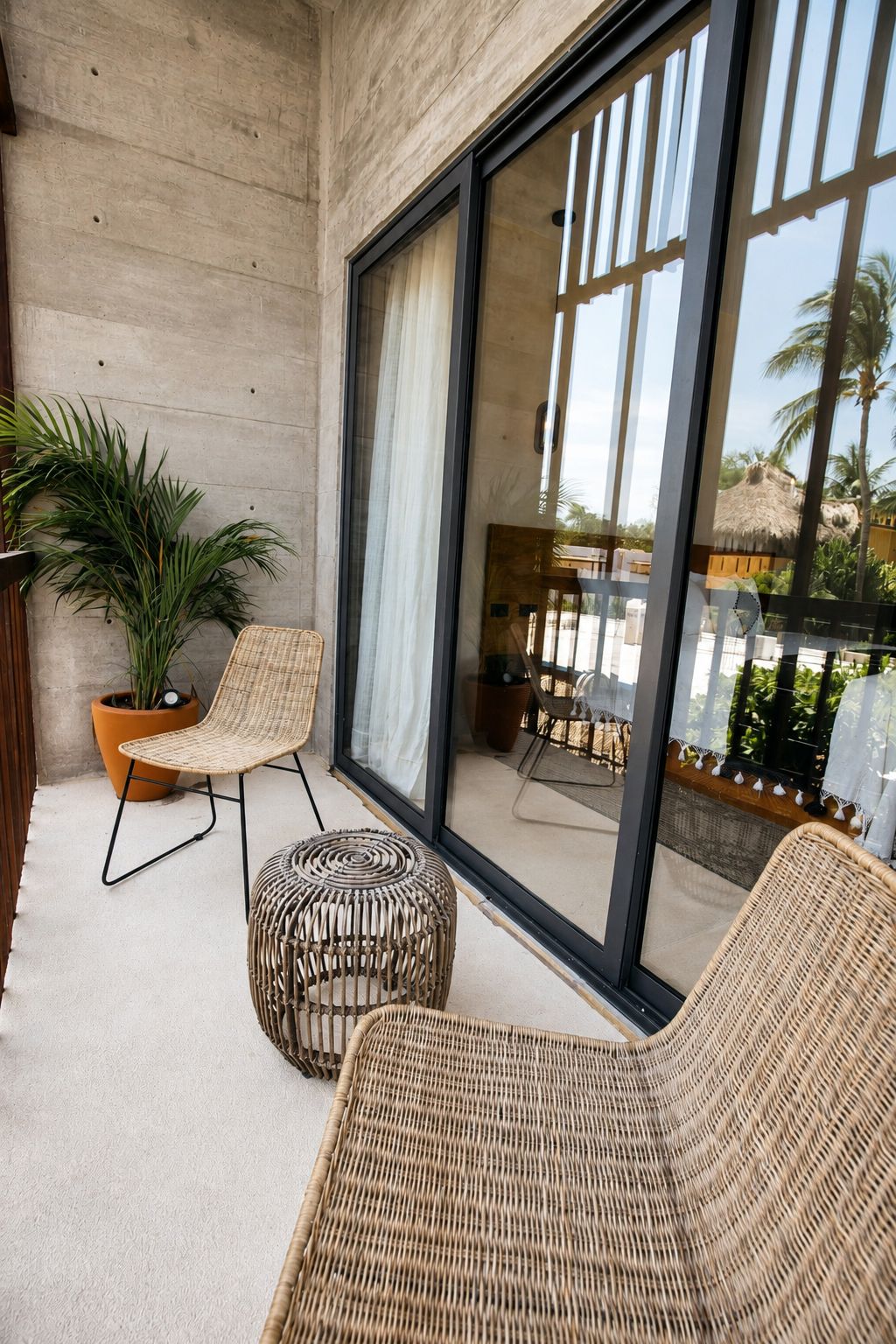 Un balcón con muebles de mimbre, una planta en maceta y vista a una construcción con techo de paja.