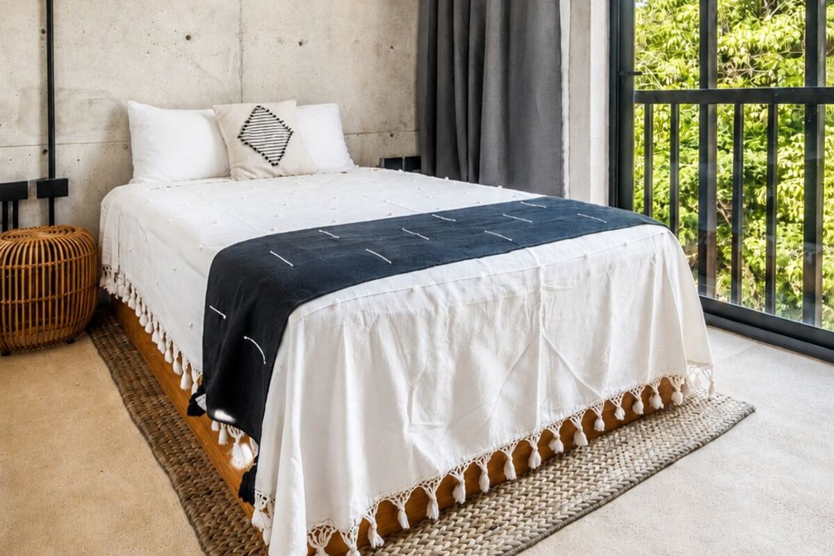 Un dormitorio con una cama grande, una pared de hormigón, vistas a la vegetación y un balcón.