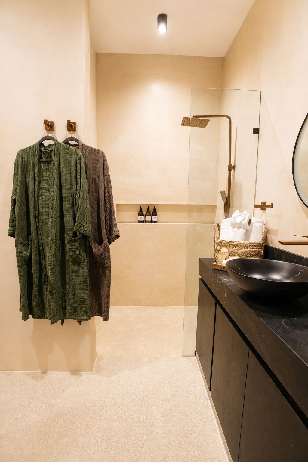 Un baño moderno con un espejo grande, un lavamanos negro y un perchero con dos albornoces.
