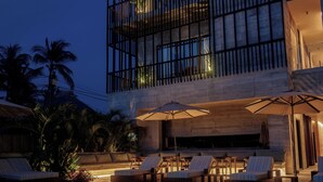 Un edificio moderno con piscina, sillas de descanso y palmeras.