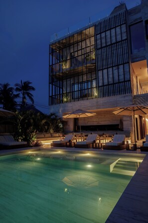 Un edificio moderno con piscina, sillas de descanso y palmeras.