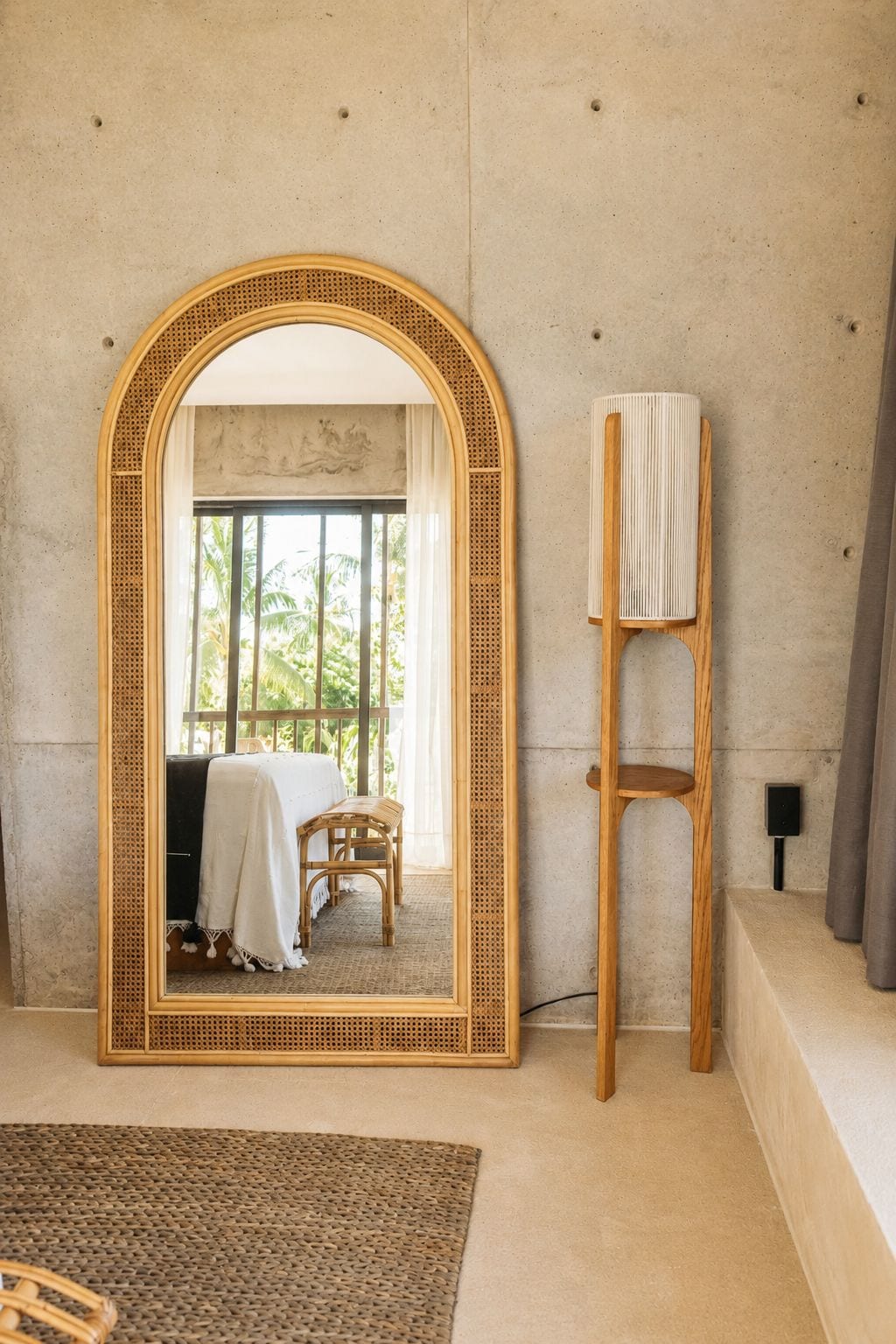 Una habitación con un espejo grande, una silla de ratán y una pequeña mesa de madera.