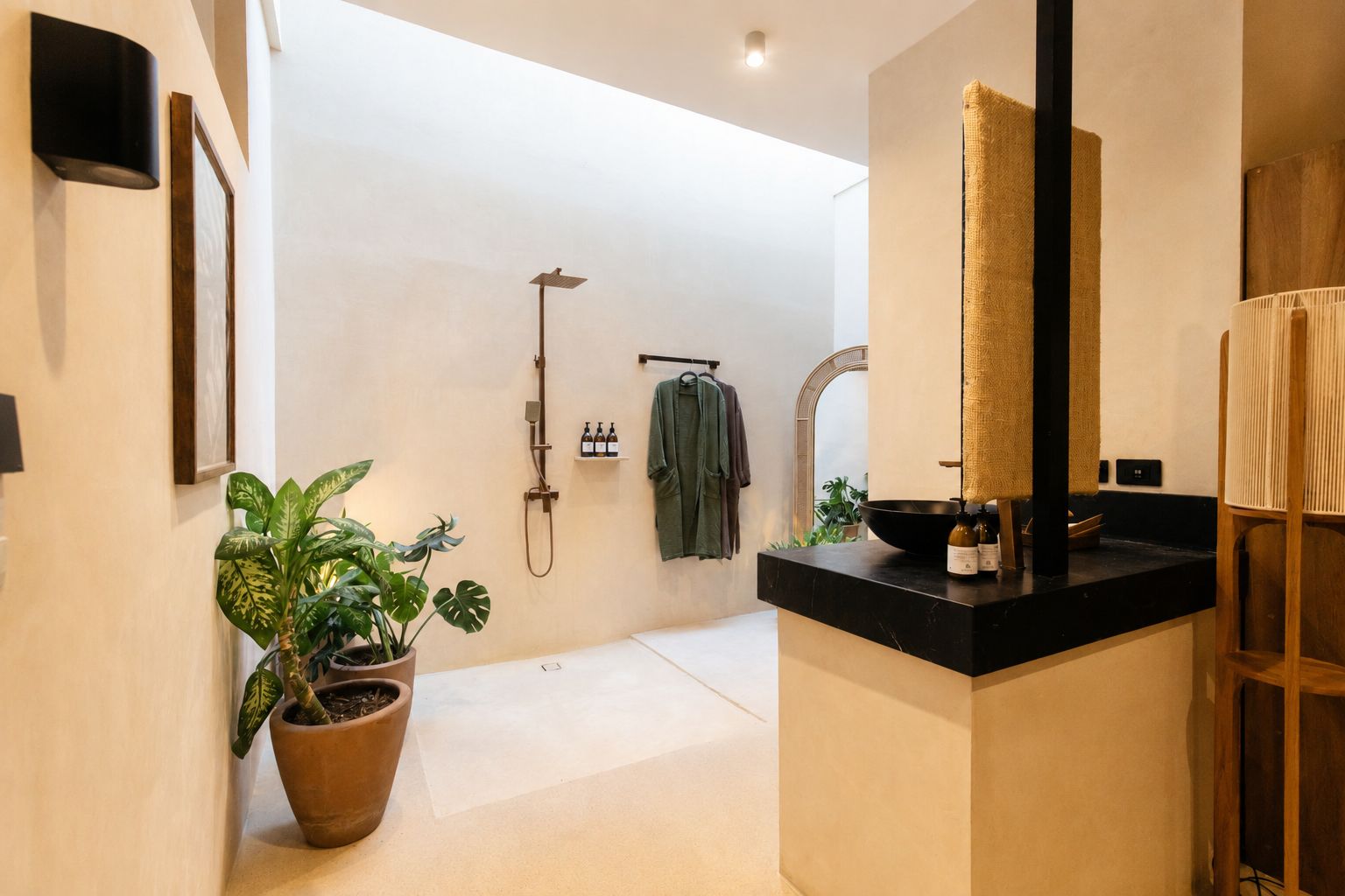 Un baño moderno con encimera negra, un espejo grande, una ducha y una planta en maceta.