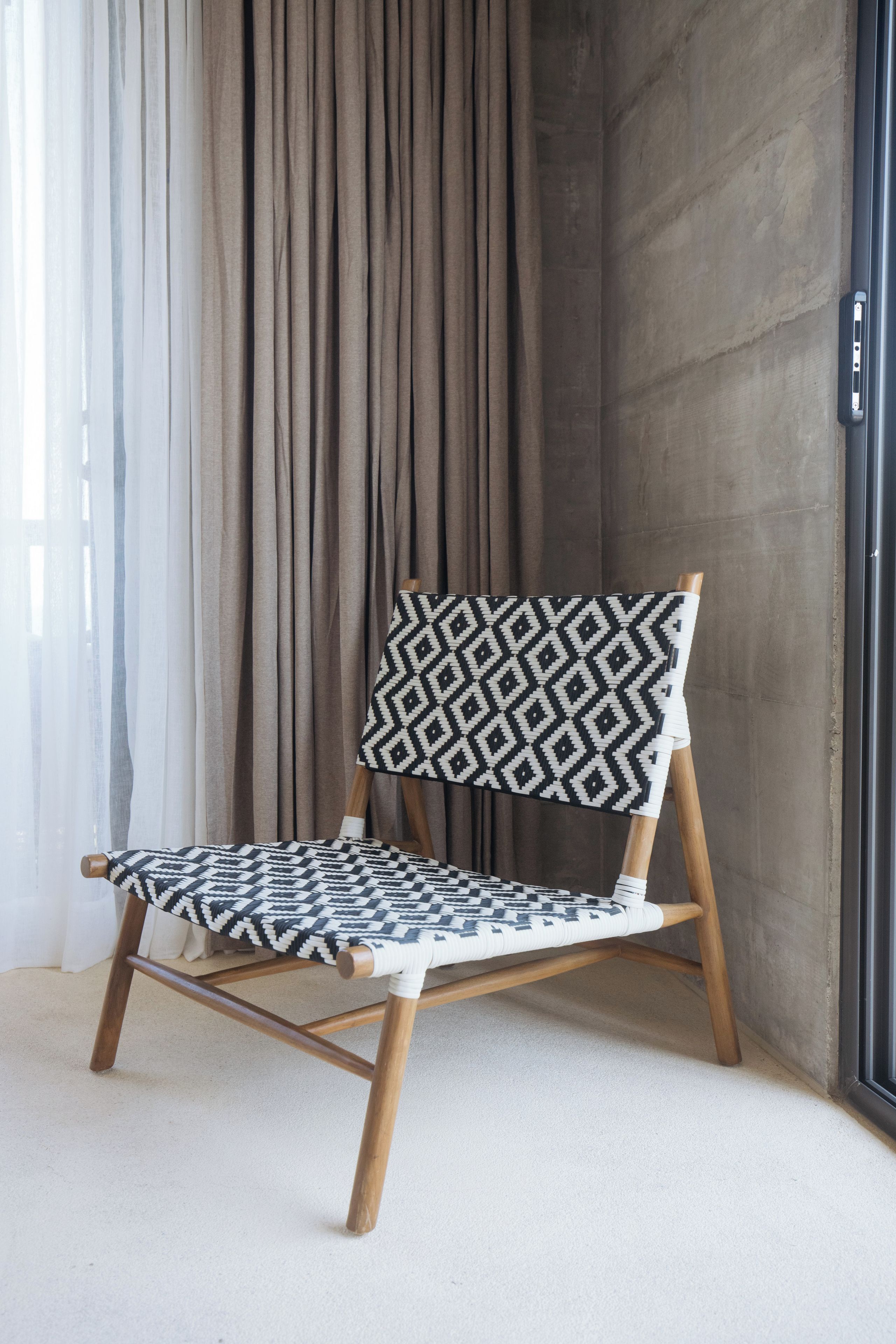 A chair with a geometric patterned backrest and seat, positioned against a wall with a curtain.