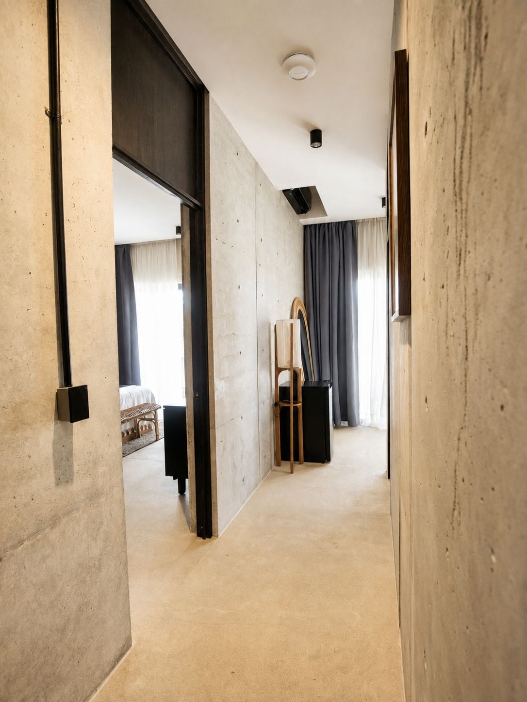 A hallway with a bed, a chair, a small table, and a mirror.