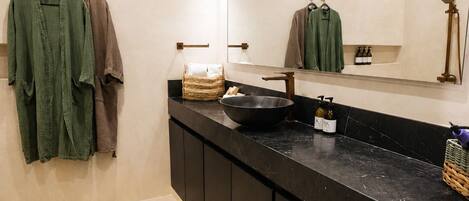 Un baño moderno con un espejo grande, un mostrador negro y un perchero con dos toallas.
