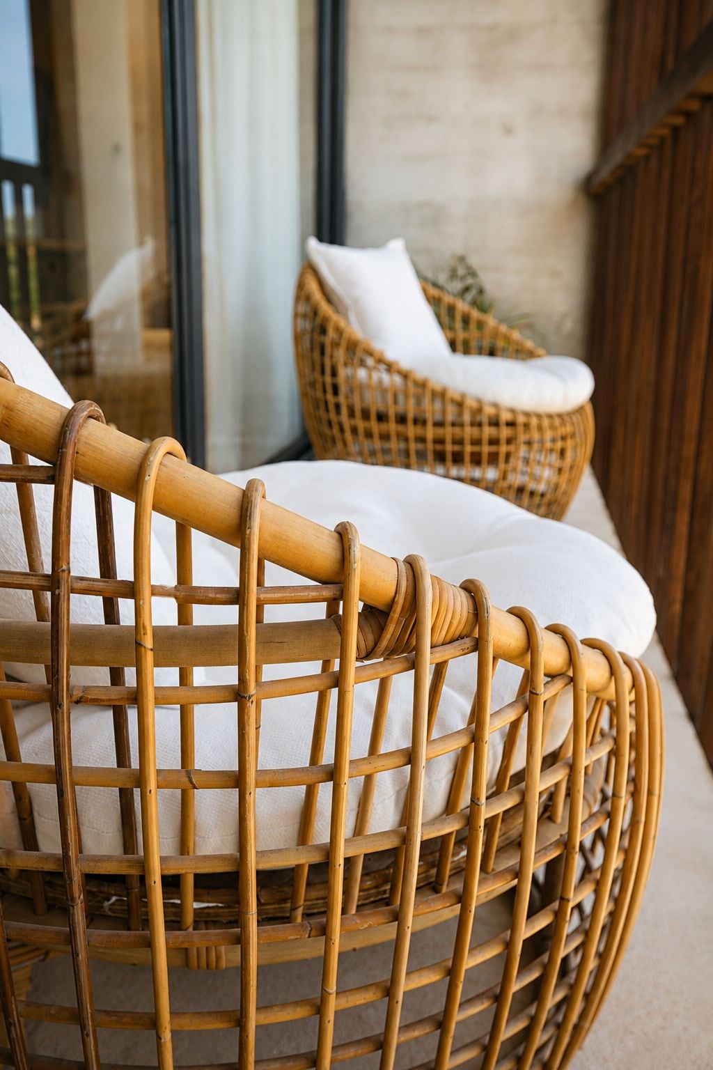 A wicker chair with a cushion, positioned near a window with a view of a building.