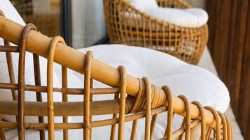 A wicker chair with a cushion, positioned near a window with a view of a building.