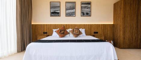 Una habitación de hotel con una cama grande, un cabecero de madera, un tapete tejido y tres cuadros en la pared.
