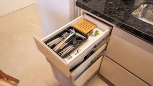 Eine Küchenschublade mit Besteck, einem Holztablett und einem kleinen grünen Gegenstand.